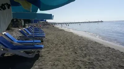 a row of blue lounge chairs on a beach with a pier at Nefeli Sea Side, Boutique Apartment in Limassol