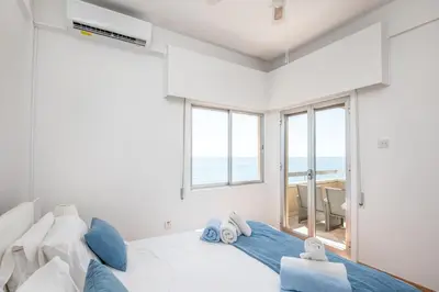 a white bedroom with a large bed with blue pillows at Apollon Sea View Beachfront Ap 302 in Larnaka