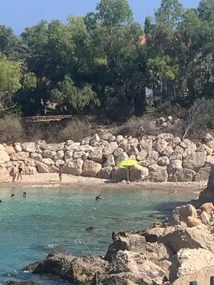 a beach with an umbrella and people in the water at One-bedroom beach apartment, 30m from an amazing beach, Coralli in Protaras