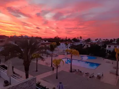 a sunset at a resort with a pool and palm trees at NISSI BEACH AYIA NAPA Pool View Apartment Large Terrace 450m from Nissi Beach in Ayia Napa