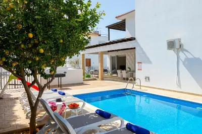 a pool with chairs and an orange tree next to a house at Protaras Sapphire Seaside Villa in Protaras