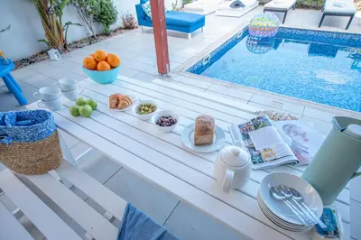 a table with plates of food next to a swimming pool at Protaras Artisan Seafront Villa in Protaras