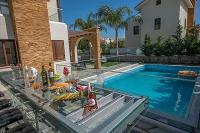 a table with food and drinks on a glass table in front of a pool at Ayia Napa Ionion Seaside Villa in Ayia Napa