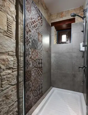 a bathroom with a shower with a stone wall at Oinoessa Traditional Boutique Guest Houses in Lofou