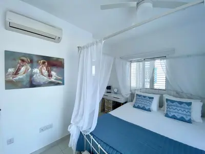 a white bedroom with a blue bed and a window at Villa Kapparis Sunrise in Paralimni