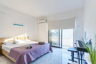 a white bedroom with a bed and a piano at Fanta Sea Apartment in Larnaka