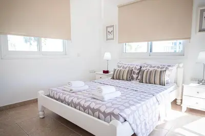 a white bedroom with a bed and two windows at Protaras View Villas in Protaras