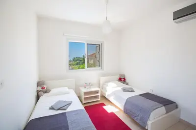 two beds in a white room with a red rug at Kalamies Family Villa in Protaras
