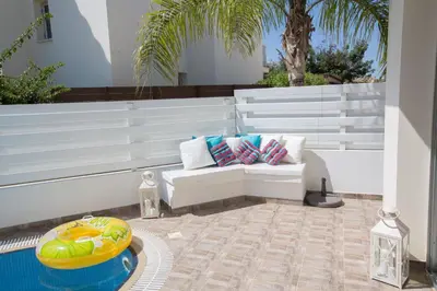 a patio with a white bench and a pool at Kalamies Family Villa in Protaras