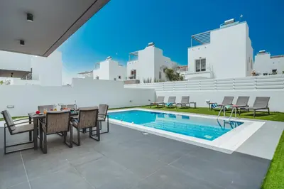 a patio with a table and chairs next to a swimming pool at Stay in Style in Modern 3 Bedroom Villas Near Nissi Beach & Square in Ayia Napa
