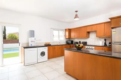 a kitchen with wooden cabinets and a washer and dryer at Voroklini Villa with Pool in Larnaka