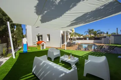 a backyard with white chairs and a table and an umbrella at Tsokkos Family Villa - Pool Garden 2' Walk to Beach in Protaras