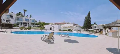 a swimming pool with two chairs in front of a house at STAY Symphony Apartment in Protaras
