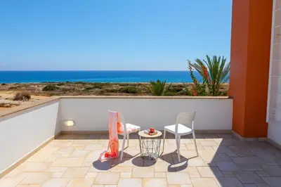 a balcony with two chairs and a table and the ocean at Protaras Seafront Villa Violetta in Protaras
