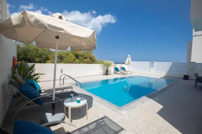 a swimming pool with an umbrella and chairs and a table at Romeo & Juliet in Protaras