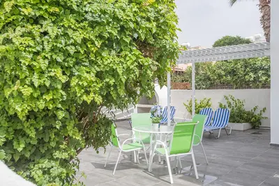 a patio with a table and chairs under a hedge at Merab Holidays Apartment Castalia 62 in Ayia Napa
