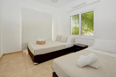 two beds in a white room with a window at Nissi Villa Ourania in Ayia Napa