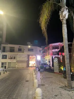 a person walking down a street at night with a palm tree at 2 bedroom apt in Ermou 4 minute walk beach in Larnaka