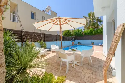a patio with an umbrella and chairs and a pool at Villa Lela Serena by Ezoria Villas in Protaras