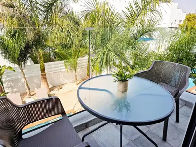 a glass table and chairs on a balcony with palm trees at Villa Green garden in Ayia Napa