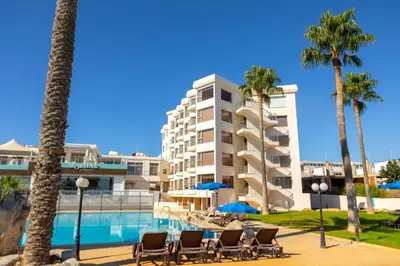 a hotel with chairs and palm trees and a swimming pool at Protaras Pallini 201 Seaside Suite in Protaras