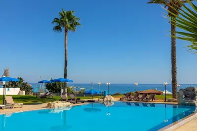 a pool with palm trees and the ocean in the background at Protaras Pallini 201 Seaside Suite in Protaras