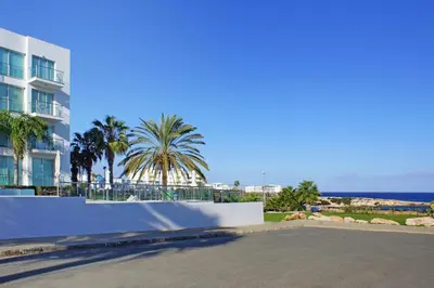 a street in front of a building with palm trees and the ocean at Niovi - Coralli Beachfront Apartment in Protaras