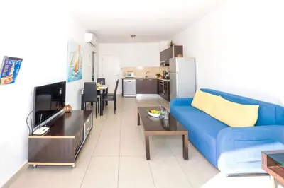 a living room with a blue couch and a kitchen at SHARON - Coralli Beachfront Apartment in Protaras