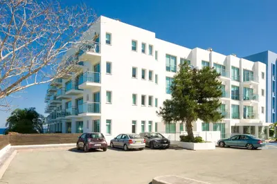 a white building with cars parked in a parking lot at ALICIA - Coralli Beachfront Apartment in Paralimni