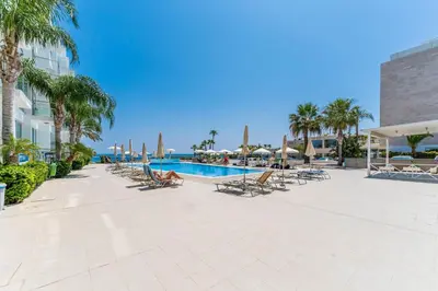 a resort with a pool and chairs and palm trees at BLISS - Coralli Beachfront Apartment in Protaras