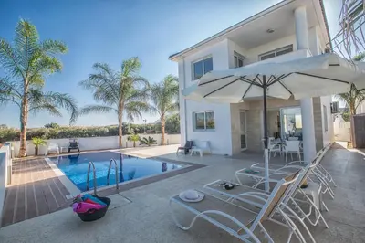a house with a swimming pool with chairs and an umbrella at Flouressia Gardens Villas in Protaras