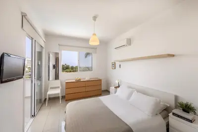 a white bedroom with a bed and a television at Flouressia Gardens Villas in Protaras