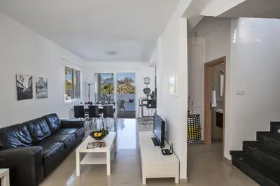 a living room with a black leather couch and a tv at Flouressia Gardens Villas in Protaras