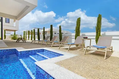 a pool with chairs and a table next to a house at Villa Amity in Protaras