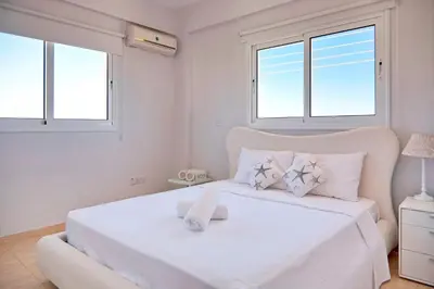 a white bedroom with a large white bed with windows at Velomar Villa in Paralimni