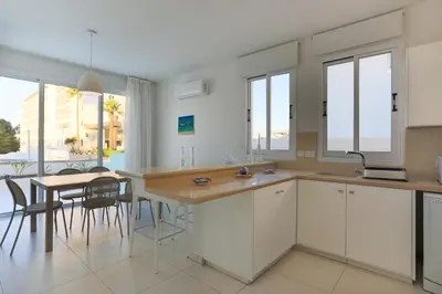 a kitchen with white cabinets and a table with chairs at Pernera Gardens Villa in Protaras