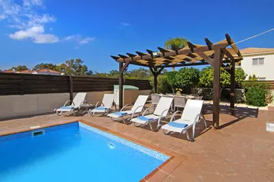 a swimming pool with chairs and a wooden pergola at Nissi Dreams Villa in Ayia Napa