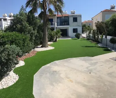 a green yard with a palm tree and a house at Beach Front Periyiali Gardens in Pervolia