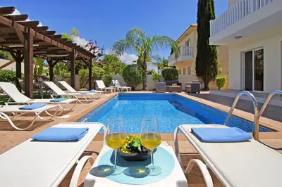 a villa with a swimming pool and two glasses of wine at Nissi Adamite Villa in Ayia Napa