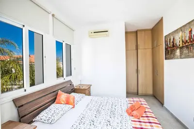 a bedroom with a bed with orange pillows and windows at Villa Mesogeios ME25 in Protaras