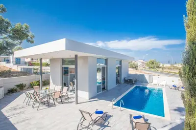 a patio with a pool and chairs and a house at Villa Polymnia Protaras 1 in Protaras