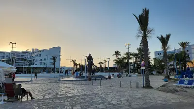 a plaza with a statue and palm trees and buildings at Ayia Napa sea view great location bars & beach in Ayia Napa