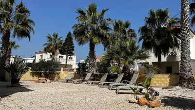 a row of chairs sitting on a beach with palm trees at Sunset Sea View Villa in Ayia Napa