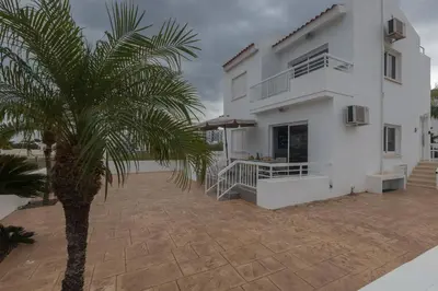 a white house with a palm tree in front of it at Sun & Sea Seaview Apartment in Protaras