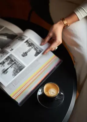 a woman is reading a book with a cup of coffee at Heart Hotel in Limassol