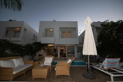 a patio with a white umbrella and chairs and a house at Jasmine Sea Front Villa in Protaras