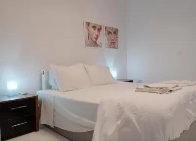 a bedroom with a bed with white sheets and a nightstand at Zelea Deluxe Apartment (BREAKBOOKING CY) in Limassol