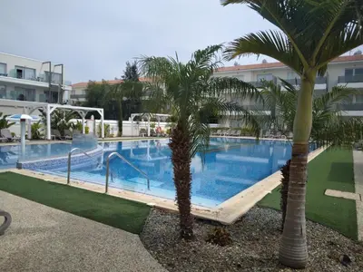 a swimming pool with two palm trees in front of a building at Sweet Retreat in Paralimni