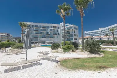 a hotel with chairs and an umbrella and palm trees at Thalassa Luxury Apartment in Protaras